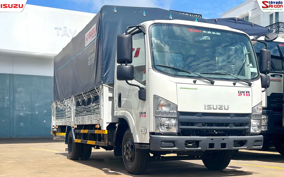 Đầu xe nhìn gần với đèn trước, lưới tản nhiệt và logo ISUZU, phía sau cabin là thùng phủ bạt