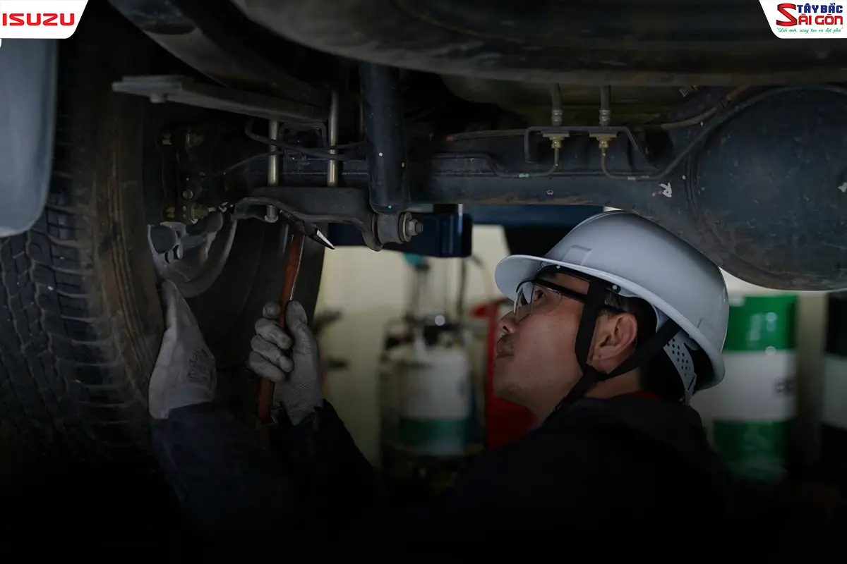 Kỹ thuật viên mặc đồ bảo hộ kiểm tra gầm xe ISUZU trong xưởng dịch vụ