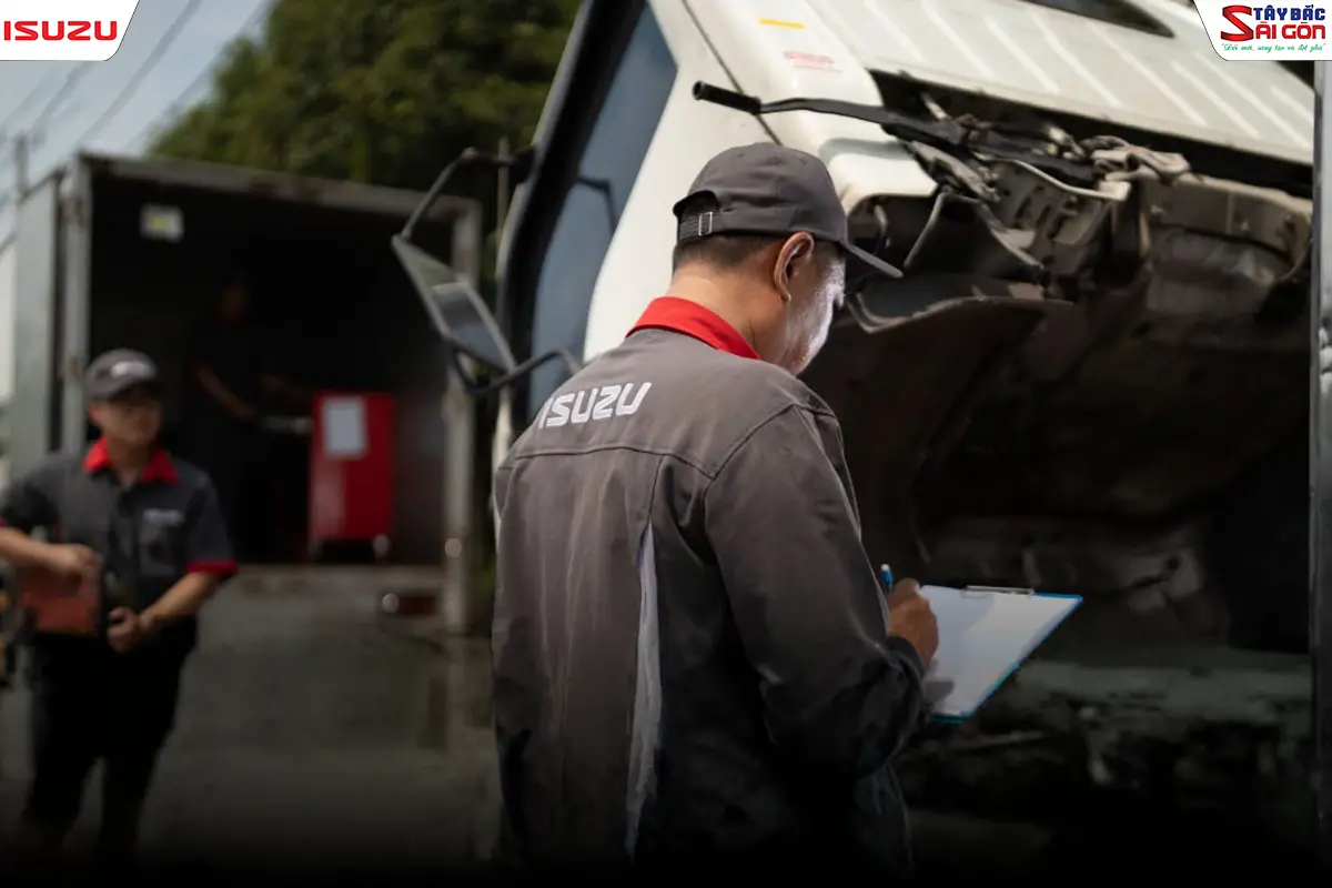 Kỹ thuật viên mặc đồng phục ISUZU kiểm tra khoang máy xe tải và ghi chú vào phiếu